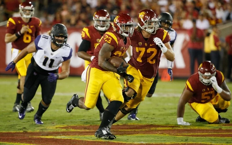 Tre Madden #23 of the USC Trojans runs the ball in the first half with help from Chad Wheeler #72 of the USC Trojans as K.J. Carta-Samuels #11 of the Washington Huskies pursues him during a game at Los Angeles Memorial Coliseum on October 8, 2015 in Los Angeles, California. The Washington vs USC Betting Odds are set.